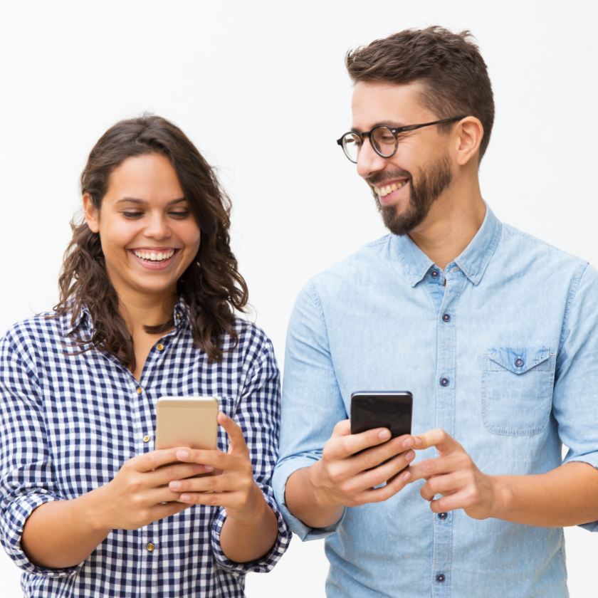 man and woman laughing while looking at cellphones